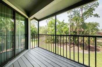 A balcony with a black railing and sliding glass doors overlooking a grassy area